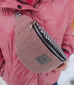 Różowa nerka o półokrągłym kształcie, wykonana z miękkiej, strukturalnej tkaniny. Posiada czarny zamek, regulowany pasek we wzór pepitki oraz metalowe detale. Noszona na skos, stylowa i praktyczna.