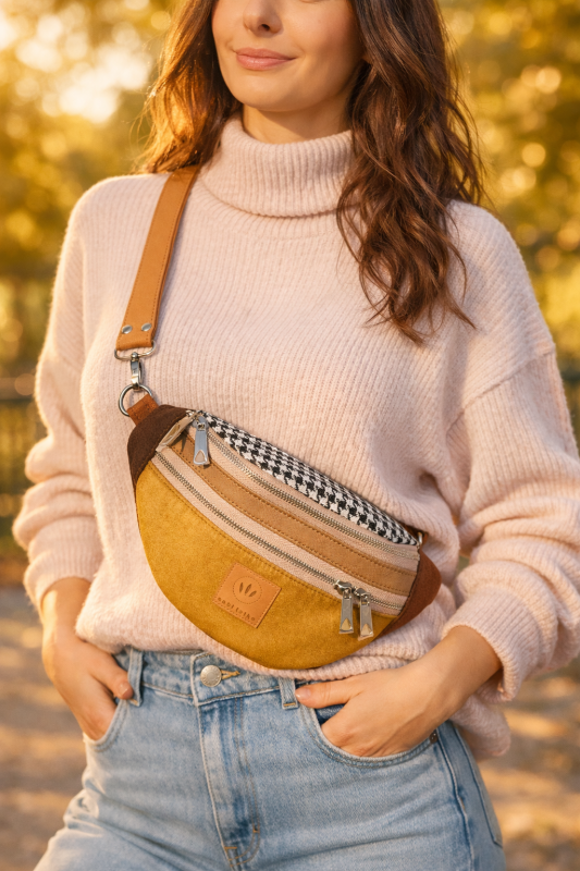 Zamszowa nerka damska w kolorze musztardowego brązu, z regulowanym paskiem i praktycznymi kieszeniami na zamek. Stylowa, miękka w dotyku, idealna do miejskich i casualowych stylizacji.
