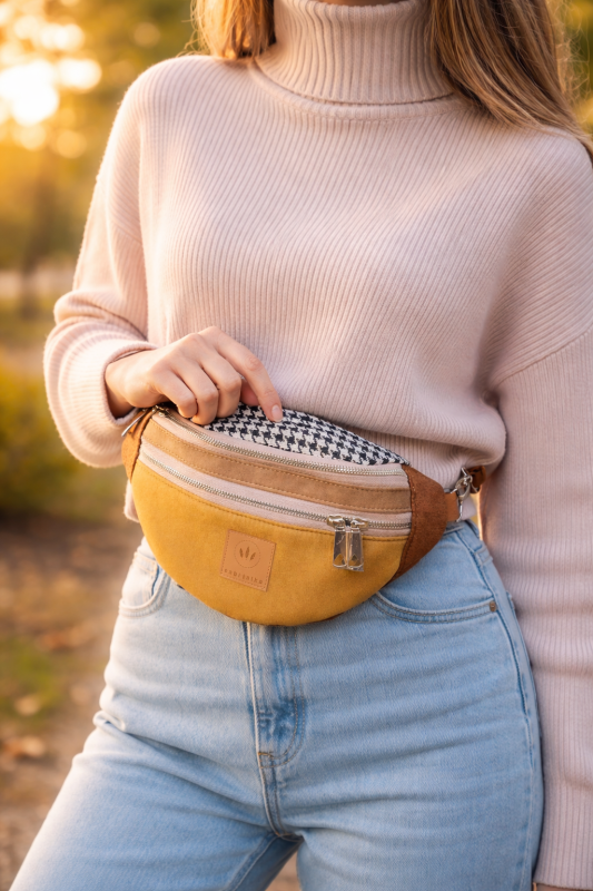 Zamszowa nerka damska w kolorze musztardowego brązu, z regulowanym paskiem i praktycznymi kieszeniami na zamek. Stylowa, miękka w dotyku, idealna do miejskich i casualowych stylizacji.