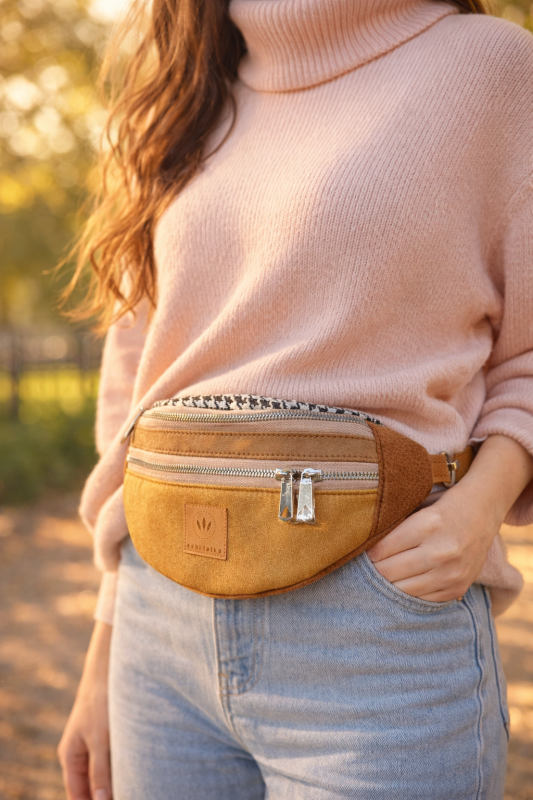 Zamszowa nerka damska w kolorze musztardowego brązu, z regulowanym paskiem i praktycznymi kieszeniami na zamek. Stylowa, miękka w dotyku, idealna do miejskich i casualowych stylizacji.