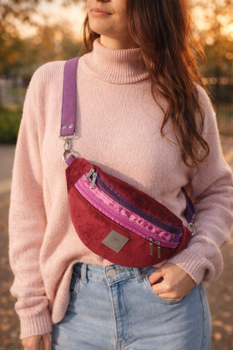 Kolorowa welurowa nerka o modnym półokrągłym kształcie, z regulowanym paskiem. Miękka faktura, bordowy kolor z różowymi akcentami i praktyczne kieszenie czynią ją stylowym dodatkiem lifestyle na co dzień.