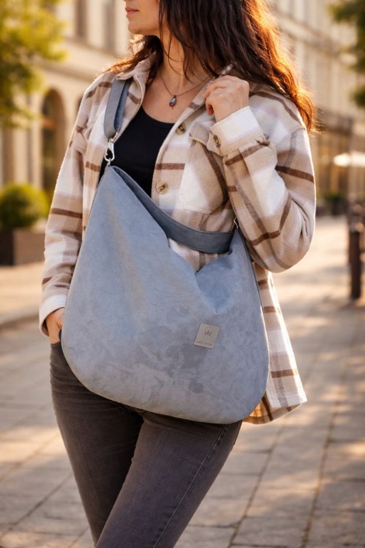 Zamszowa torba hobo w eleganckim, miejskim stylu. Miękka, lekka i pojemna, idealna na co dzień. Ponadczasowy kształt, naturalna faktura zamszu i wygodne noszenie na ramieniu. Stylowa torba damska do miasta.