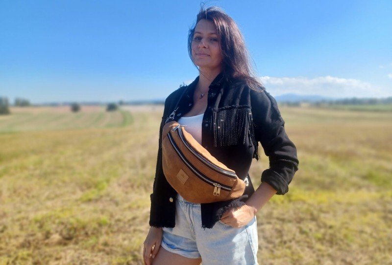 Duża nerka z naturalnego zamszu w kolorze brązowym karmelowym. Stylowa, pojemna i wygodna, z podwójnym zamkiem i regulowanym paskiem. Idealna do codziennych stylizacji i looków lifestyle.