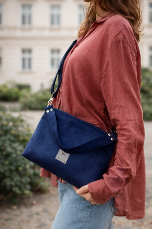 Mała zamszowa torebka w kolorze głębokiego granatu, elegancka i funkcjonalna. Miękka faktura, regulowany pasek i minimalistyczny design sprawiają, że idealnie pasuje do codziennych i eleganckich stylizacji.