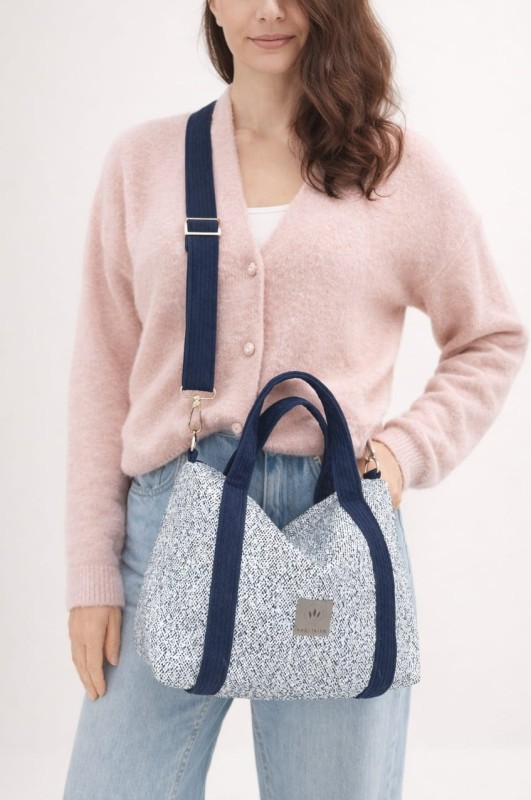 Stylowa torebka z plecionki o eleganckim, prostokątnym kształcie. Jasnoniebieska struktura z granatowymi uchwytami i regulowanym paskiem łączy naturalną fakturę z nowoczesnym designem. Lekka, pojemna i idealna na co dzień.