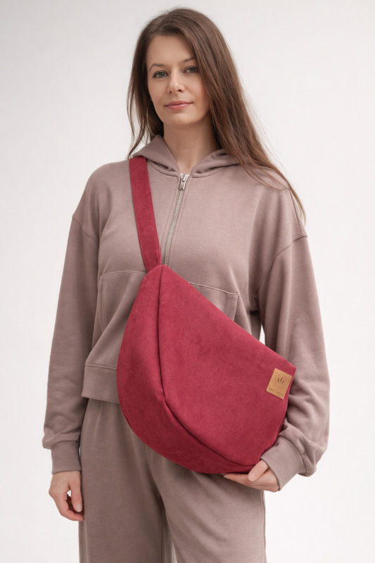 Zamszowa torba hobo w głębokim, czerwonym kolorze. Miękka, pojemna i lekka, z wygodnym paskiem na ramię. Stylowy, półokrągły kształt i minimalistyczny design sprawiają, że idealnie dopełnia miejskie i casualowe stylizacje.