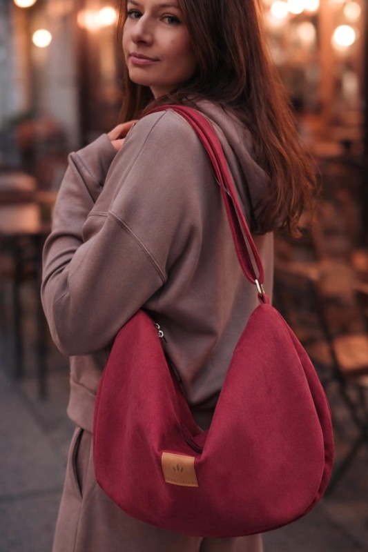 Zamszowa torba hobo w głębokim, czerwonym kolorze. Miękka, pojemna i lekka, z wygodnym paskiem na ramię. Stylowy, półokrągły kształt i minimalistyczny design sprawiają, że idealnie dopełnia miejskie i casualowe stylizacje.