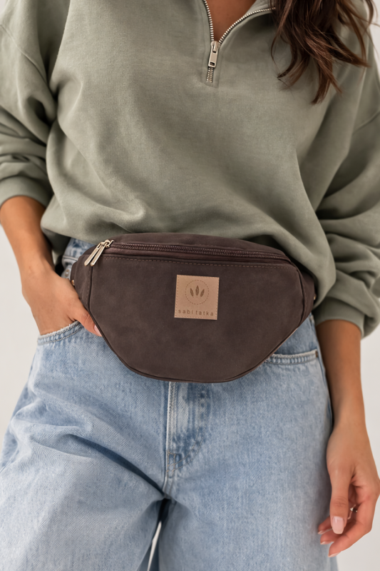 Czekoladowa zamszowa nerka to stylowy i praktyczny dodatek na co dzień. Miękka faktura, modny fason i wygodny pasek sprawiają, że idealnie sprawdzi się w miejskich stylizacjach, zapewniając komfort noszenia i elegancki wygląd.