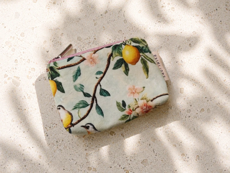 Małe etui na karty i monety w cytrusowo-kwiatowy wzór z pastelowym zamkiem. Lekkie, poręczne i stylowe – idealne do przechowywania kart, gotówki i drobiazgów. Naturalny design inspirowany śródziemnomorskim stylem.