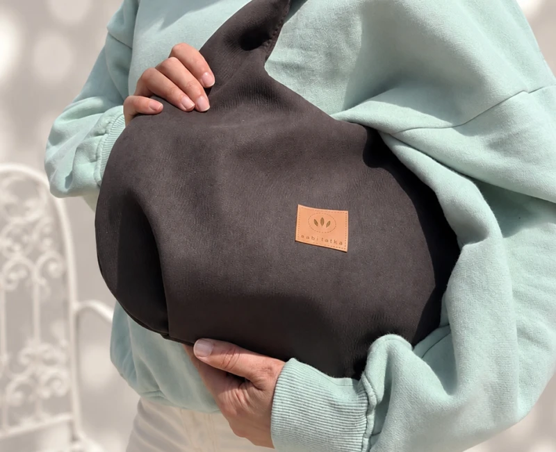 Zamszowa torebka hobo w ciemnobrązowym kolorze to połączenie minimalistycznego designu i funkcjonalności. Miękka faktura, pojemne wnętrze i wygodny pasek na ramię sprawiają, że idealnie sprawdzi się w codziennych stylizacjach casual i smart casual.