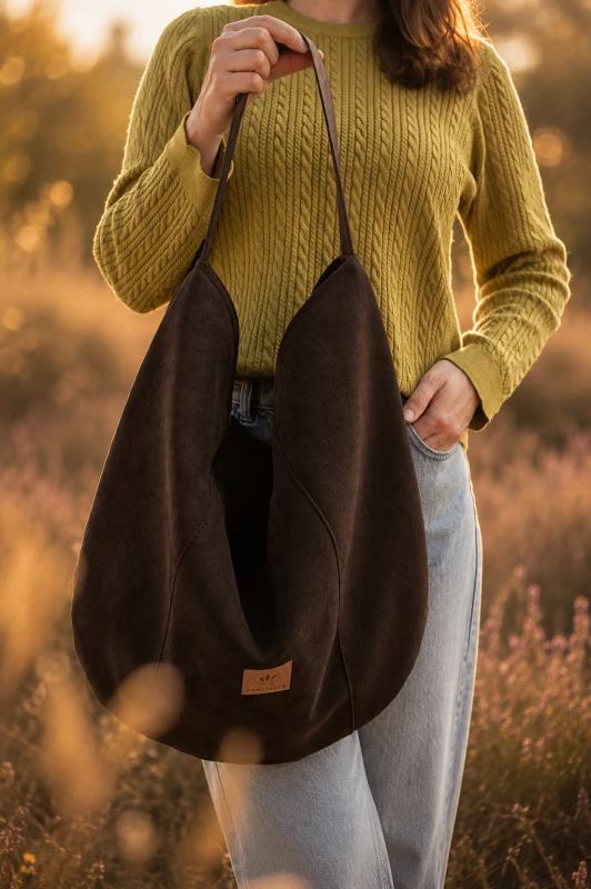 Zamszowa torba hobo w kolorze czekoladowego brązu, lekka i stylowa. Pojemna forma, minimalistyczny design i naturalna faktura sprawiają, że idealnie uzupełnia codzienne i letnie stylizacje.