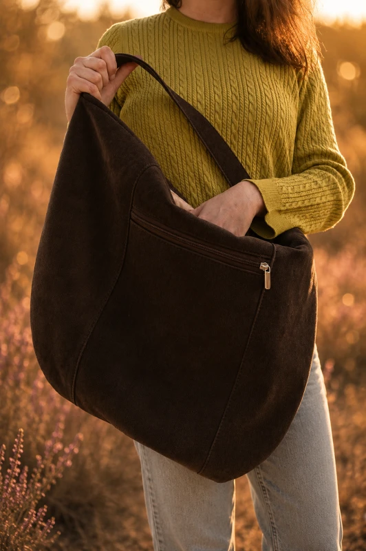 Zamszowa torba hobo w kolorze czekoladowego brązu, lekka i stylowa. Pojemna forma, minimalistyczny design i naturalna faktura sprawiają, że idealnie uzupełnia codzienne i letnie stylizacje.